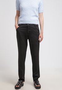 Pantaloni neri su misura dal tessuto morbido, con chiusura frontale a bottoni e tasche laterali. Abbinati a un top corto a maniche corte di un delicato blu fuzzy.