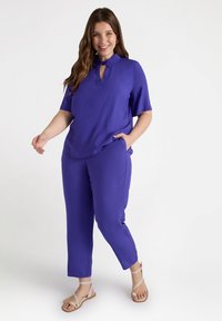 Paars twee-delig outfit met een kortärmige top met een kraag en een keyhole-detail, en bijpassende relaxte broek. Soepele textuur.