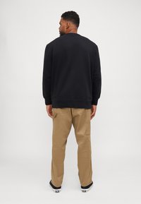 Svart sweatshirt med rund halsringning och ribbade ärmslut, tillsammans med bruna cargobyxor med sidofickor och en avslappnad passform.