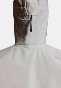 Vue arrière d'une veste à capuche beige clair avec un cordon de serrage noir réglable et un stoppeur sur la capuche.