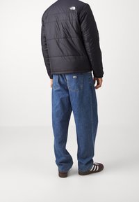 Svart puffjacka med kviltat mönster, tillsammans med löst sittande blå denimjeans. Bruna skor och vitrandiga detaljer på skorna.