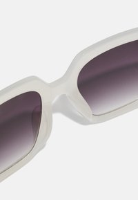 Sunglasses med en gjennomsiktig hvit ramme og gradient mørke linser. Strømlinjeformet, angulær design med en jevn tekstur og fremtredende form.