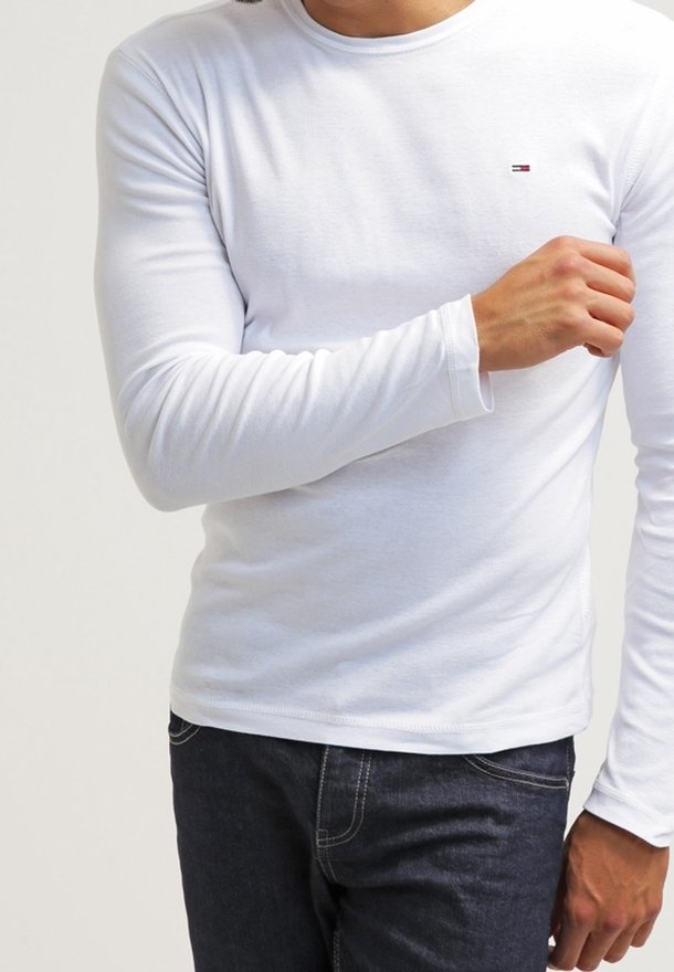 Camiseta blanca de manga larga con cuello redondo, hecha de algodón. Presenta un pequeño logo rojo y azul en el pecho y mangas ajustadas.