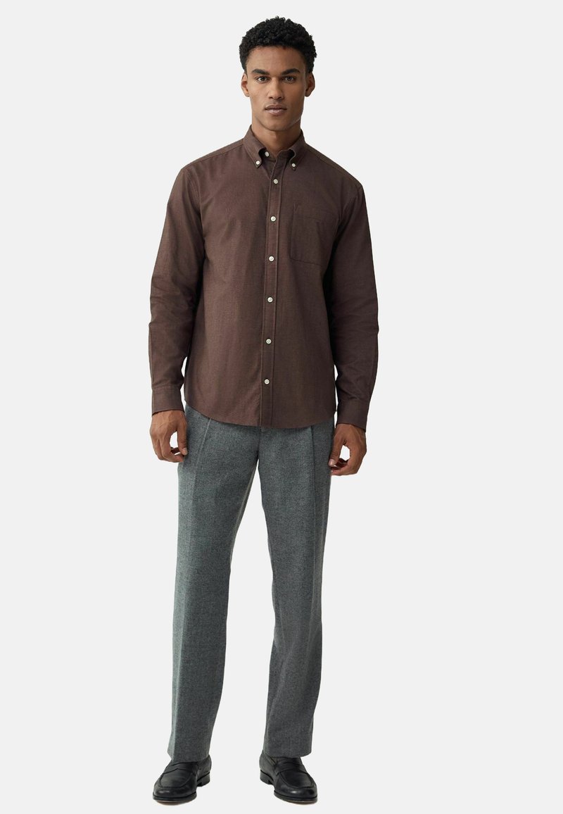 Brun knappad skjorta med ficka, tillsammans med grå strukturerade byxor och svarta skor. Klädseln har en skräddarsydd passform och klassisk design.