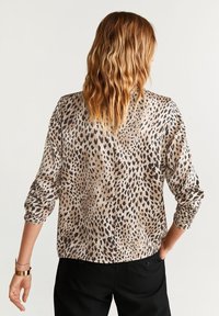 Bluse im Leopardenmuster mit glatter Textur, langen Ärmeln und lockerer Passform, kombiniert mit schwarzen Hosen. Die Rückansicht zeigt Detail über das Muster.