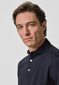 Marinblå polo med tre knappar, en strukturerad krage och korta ärmar. Slät bomullstyg med sömnadsdetaljer.