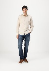 Cămașă bej cu nasturi, blugi albaștri, teniși maro. Design simplu, croială obișnuită, textură netedă. Fără modele sau grafice vizibile.