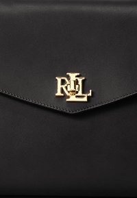 Black leather clutch with a flap closure, featuring a gold-tone logo accent in the center. Smooth texture and minimalistic design.