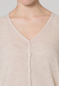 Cardigan beige chiaro con scollo a V, texture a coste sulle maniche e cinque bottoni coordinati sul davanti. Tessuto morbido e leggero.