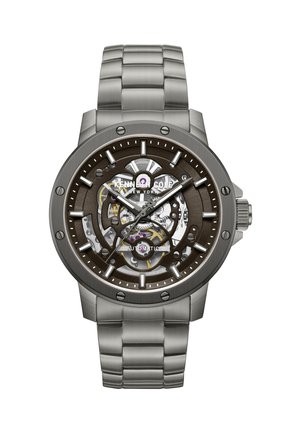 Herreur i rustfrit stål med automatisk urværk og skeletskive, der viser indre tandhjul, selvlysende timeviser og metalarmbånd med led.