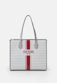Sac fourre-tout en blanc et gris avec un motif géométrique, des accents rayés rouges et crème, des poignées en cuir, et un logo avec l'année de création.