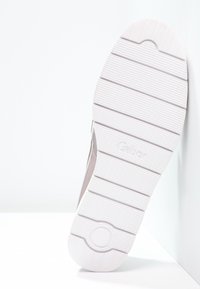Vit sneakersula med ett strukturerat mönster av horisontella ribbor och cirkulära accenter, med en upphöjd logotyp och släta kanter.