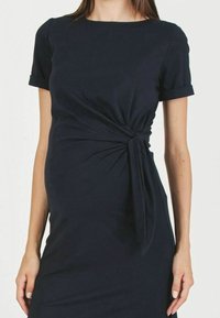 Marinblå klänning i elastisk tyg med korta ärmar, rund halsringning och knutdetalj i midjan för att framhäva formen.