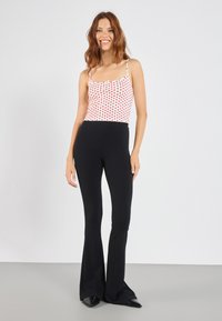 Red and white polka dot tank top with spaghetti straps, paired with fitted black ribbed flared pants and black pointed-toe shoes.