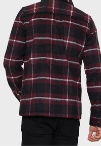 Punainen ja musta ruudullinen flanellikoshirtti valkoisilla viivoilla, pehmeä rakenne, nappikiinnitys hihansuissa ja suora helma, perinteinen kaulus.