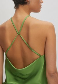 Groene zijden cami-top met dunne gekruiste bandjes, die een gladde rug onthullen, en een slanke, vloeiende textuur. Verstelbare banddetails zijn opgemerkt.