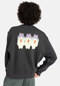 Donkergrijze sweatshirt met een ronde hals en ribgebreide manchetten, voorzien van een kleurrijke bloemenafbeelding op de achterkant met lachende gezichten.