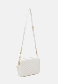 Bílá prošívaná kabelka obdélníkového tvaru. Má odnímatelný hladký popruh a zlaté řetízkové doplňky. Zipové uzavírání na horní straně.