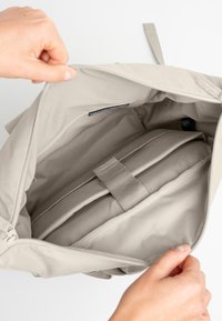 Beige Stofftasche mit mehreren Fächern im Inneren; gepolsterte Einlage mit Riemen gesichert; glatte Textur und Reißverschlussverschluss.