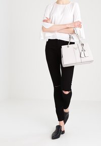 Sac à main structuré gris avec des accents argentés et un pendentif. Assorti à un chemisier blanc à manches évasées et un jean skinny noir déchiré. Sabots noirs.