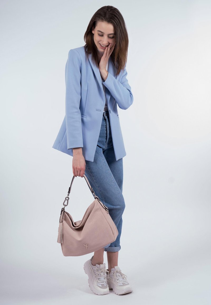 Blazer bleu clair sur un top blanc, associé à un jean bleu. Tenant un sac à main texturé rose clair avec des accents argentés et une frange. Baskets blanches.