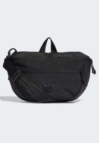 Svart tyg crossbody-väska med dragkedjor, justerbar rem och handtag upptill. Har ett präglat logo på framsidan och en slät yta.