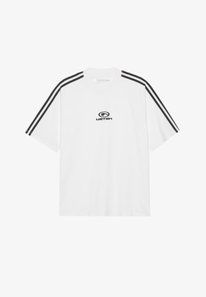 Valkoinen puuvillapaita, jossa on mustat pystysuorat raidat hihoissa ja keskellä logo. Pyöreä pääntie, lyhyet hihat ja rento leikkaus.