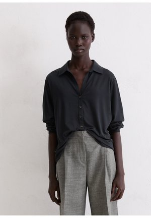 Donkergrijze button-up shirt met kraag en een relaxte pasvorm, gecombineerd met lichtgrijze, op maat gemaakte broeken. Soepele stoftextuur, minimale detailing.