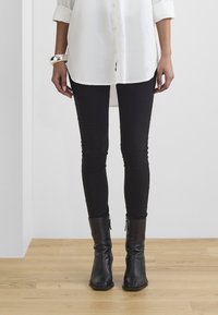 Bílá košile na knoflíky, černé slim-fit kalhoty a černé kotníkové boty se zipem na boku. Hladká tkanina a upravený silueta.