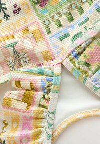 Színes tűzött anyag texturált mintázattal, pasztell rózsaszín, sárga, zöld és kék árnyalatokban. Ráncolt díszítésekkel és több színű mintákkal rendelkezik.