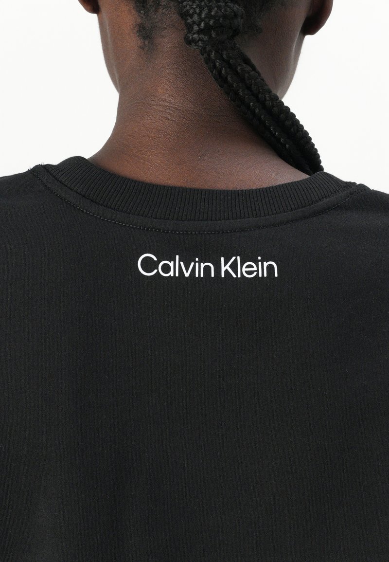 Sudadera de algodón negra con cuello acanalado, que presenta un logotipo "Calvin Klein" bordado en la parte posterior.