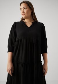 Black tiered dress with short puffed sleeves, V-neckline, textured fabric, and gathered waistline. Subtle sheen and soft drape.