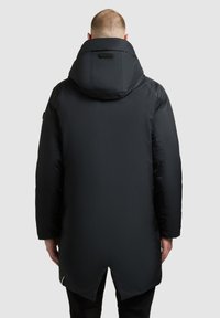 Must värvitud paks jakk kõrge kraega ja kapuutsiga. Omab sirget siluetti ja lukuga külgventile. Sile, kerge kangas.