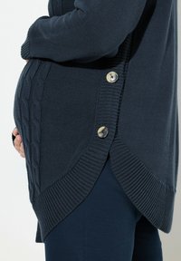 Dunkelblaues Stilloberteil mit geripptem Saum und Zopfmuster-Detail an der Seite, ausgestattet mit zwei großen Knöpfen und einem lockeren Schnitt.