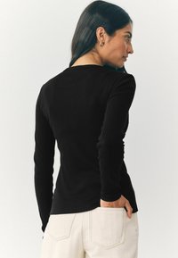 Schwarzes Langarmshirt mit figurbetontem Design und ribbeliger Textur. Der Rücken hat einen runden Ausschnitt und dezente Nahtdetails.