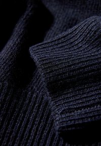 Ciemnogranatowa dzianina z prążkowaną fakturą, ukazująca miękkie włókna i subtelne różnice w odcieniach. Widok z bliska podkreśla szczegółowe wykonanie.