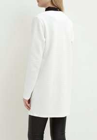 Vit texturerad lång cardigan med en något lös passform. Slät material, långa ärmar och rundad halsringning. Inga synliga knäppningar eller mönster.