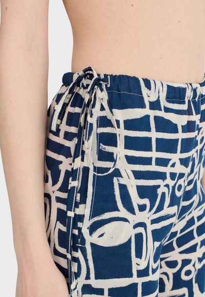 Zbliżenie na osobę noszącą niebieskie spodnie z białymi abstrakcyjnymi wzorami linii i zawiązanym sznurkiem w pasie.