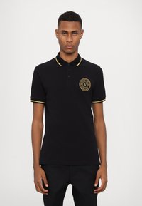 Polo shirt din bumbac negru cu accente aurii pe guler și mâneci. Prezintă un logo rotund pe partea stângă a pieptului. Croială clasică, mâneci scurte.