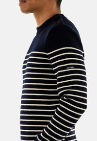 Maglione a righe blu navy e crema, con scollo a girocollo, bottoni laterali e un piccolo etichetta sul maniche sinistro.