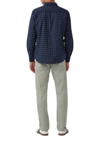 Camicia a scacchi blu con motivo a griglia bianca e beige, maniche lunghe. Pantaloni grigi chiari con vestibilità rilassata e tasche. Scarpe bianche con accenti scuri.