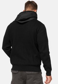 Black sweater with a textured knit design, featuring a contrasting smooth fabric hood. Fitted cuffs and hem. Back view shows subtle stitching details.