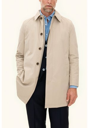 Cappotto impermeabile beige con colletto a punta, chiusura frontale con bottoni e tasche laterali. Indossato sopra una camicia blu, con una texture liscia e opaca.