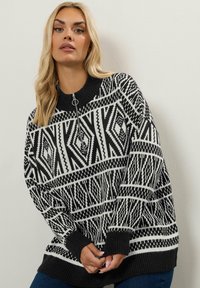 Pullover mit einem schwarz-weißen geometrischen Muster, gestrickter Textur, hohem Kragen und Reißverschluss. Oversized-Schnitt mit gerippten Bündchen.