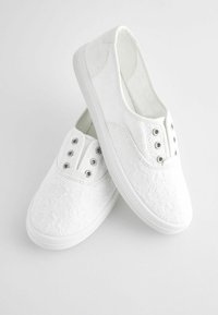 Scarpe slip-on bianche con un motivo in pizzo floreale, occhielli metallici e suola in gomma testurizzata per una buona aderenza. Design piatto e superiore senza cuciture.