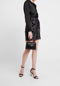 Svart minikjol med blommönster, sittande med en silkeslen svart blus med knapppdetaljer, tillsammans med en texturerad svart handväska och svarta ankelsandaler.