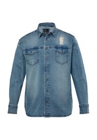 Camisa de mezclilla en azul claro con un aspecto desgastado, con cierre de botones en la parte delantera, dos bolsillos en el pecho y detalles rasgados en el hombro.