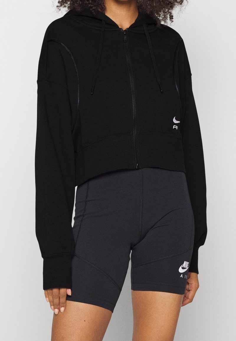 Svart kort zip-up hoodie med huva, i en slät tygkvalitet och diskreta sömnadsdetaljer, tillsammans med figurnära svarta shorts med logotypdetaljer.