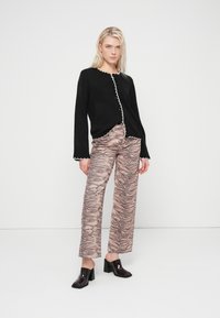 Black cardigan with white scalloped trim, paired with light pink pants featuring a dark tiger stripe pattern, and glossy black block-heeled shoes.