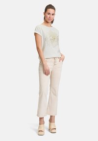 T-shirt vert clair à manches courtes avec un design graphique doré, assorti à un pantalon évasé de couleur crème et des chaussures à plateforme crème.